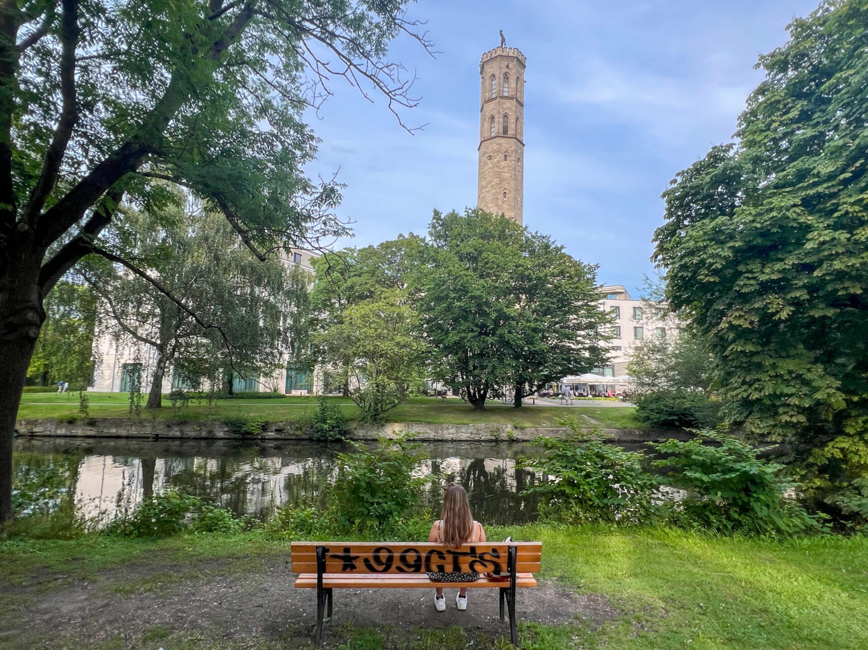 Frau auf Parkbank vor der Oker und ehemaligem Druckturm am Steigenberger Braunschweig